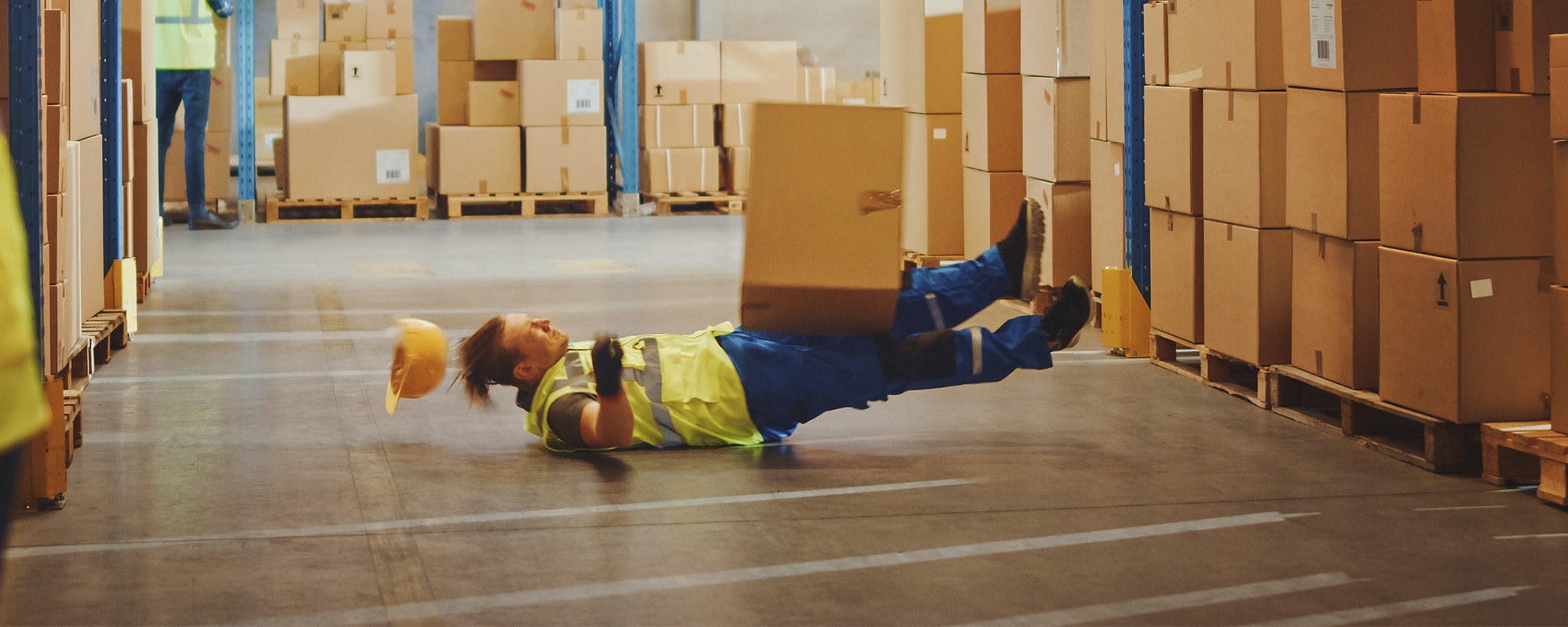 warehouse worker has work related accident falls while trying to pick up cardboard box from the shelf. colleagues call f