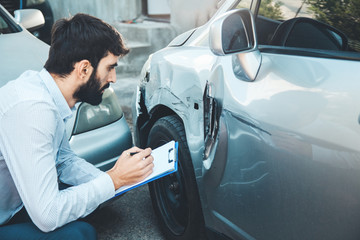 man with clipboard looking at car vehicle damage